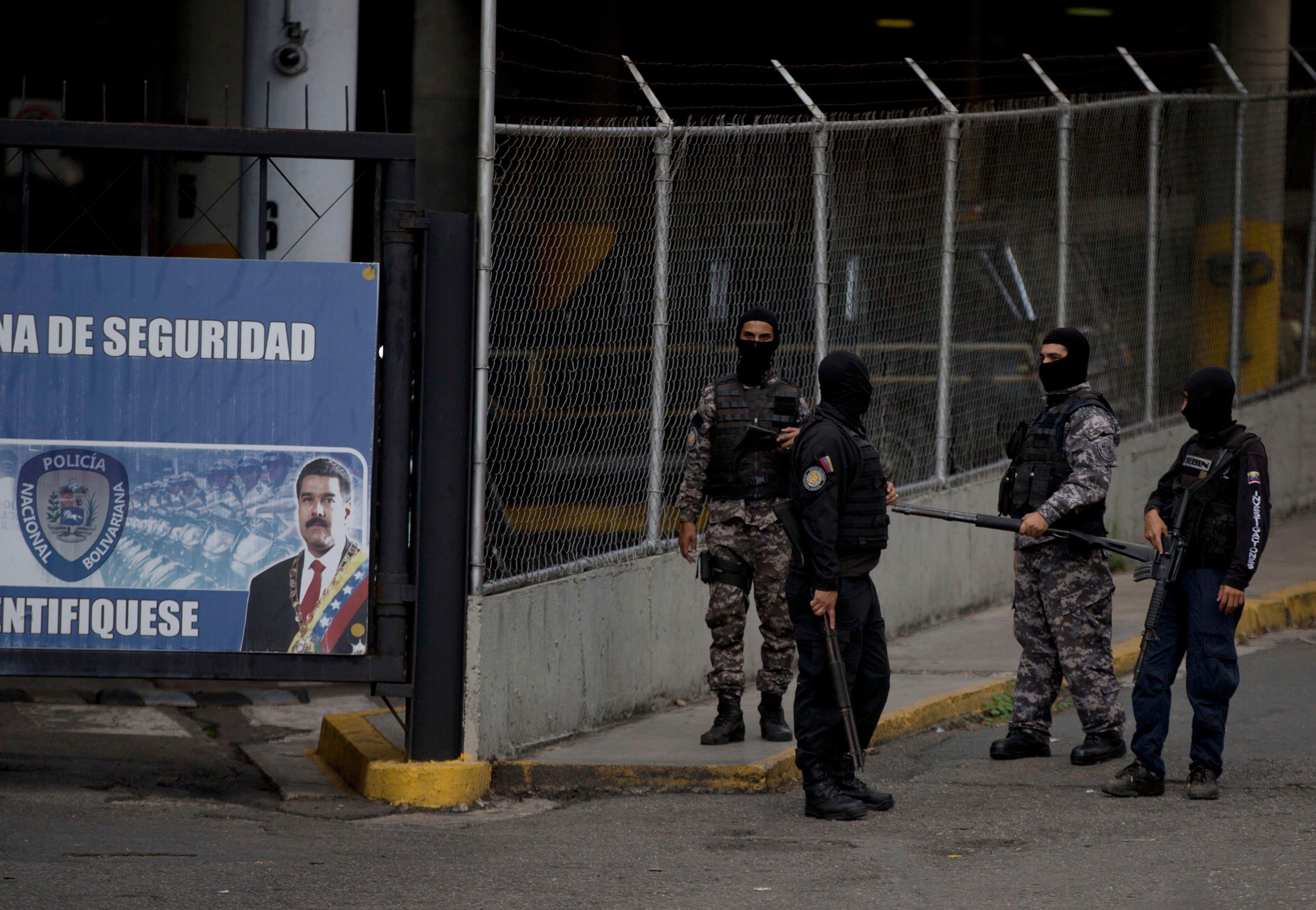 Agentes de la policía política venezolana, con sus rostros cubiertos, hacen guardia en la puerta principal de la sede del SEBIN en Caracas, Venezuela. Foto: AP/Fernando Llano/Archivo. 